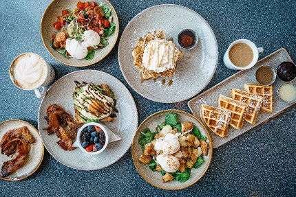 Brunch sobre una mesa con diferentes platos. Ensalada de pollo, tostada con huevo, frutas,waffles con crema.