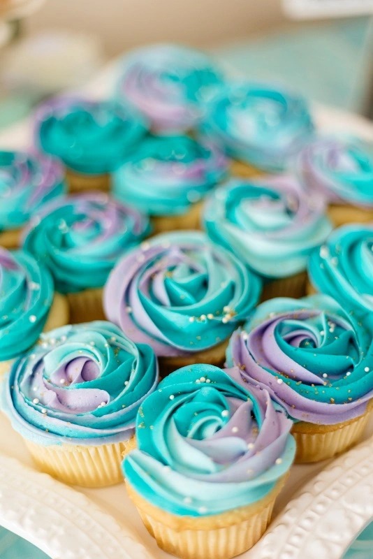 Vista de cerca a cupcakes con crema turquesa y lila.