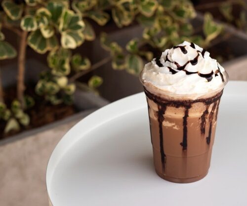 Café frío de chocolate con crema y salsa de chocolate sobre un plato blanco.